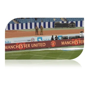 Manchester United advertising banner displayed at a stadium with security personnel in the background.
