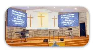 Interior view of a church featuring three wooden crosses and a projector screen with song lyrics.