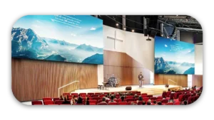 Interior view of a modern church with a stage, large screens, and seating for the congregation.