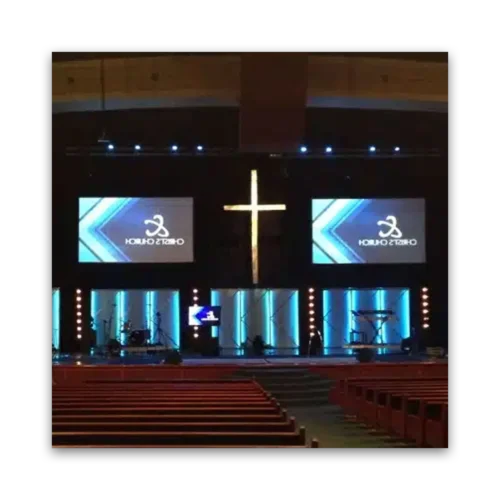 Stage setup in a church featuring a large cross and two screens displaying graphics.