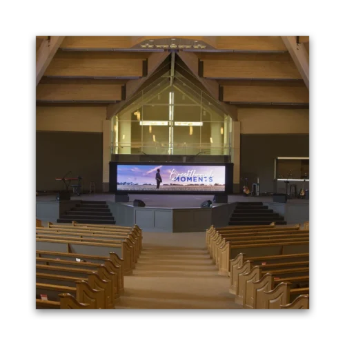 Interior view of a modern church featuring a stage with a large screen and rows of wooden seating.