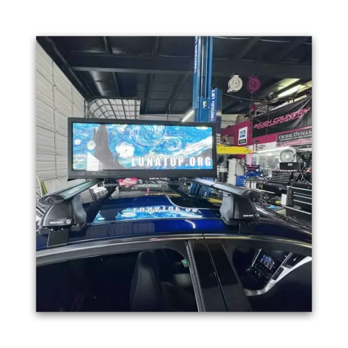 Digital display mounted on the roof of a car showing a colorful design with the text 'LUNATOP.ORG'.