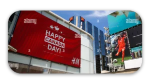 Large red billboard displaying 'Happy Canada Day!' with H&M logo in a city setting.
