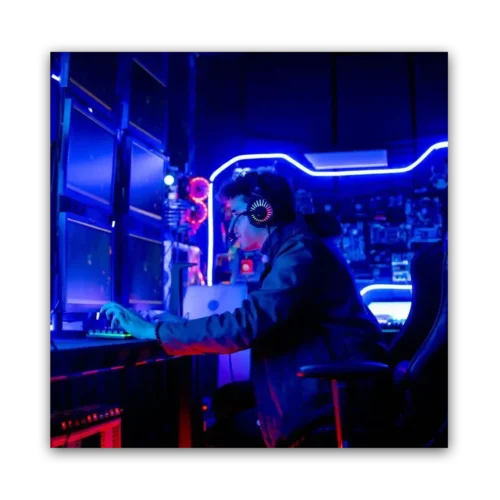 Individual wearing headphones and using a keyboard in front of multiple computer monitors in a gaming environment.